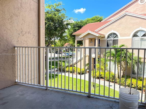 View from a balcony of a residential building with a red roof and arched windows.