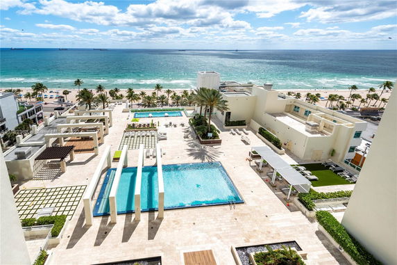 Panoramic view of a beachfront area with swimming pools and palm trees.