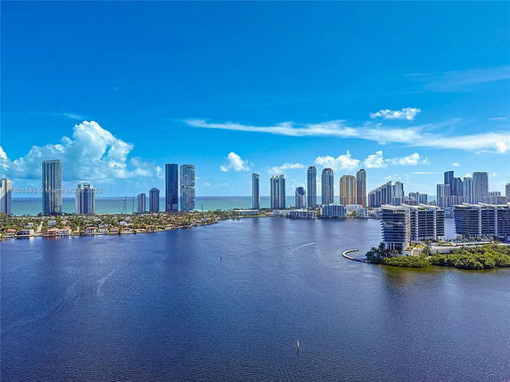 Panoramic view of a coastal city skyline with tall buildings and a large body of water in the foreground.
