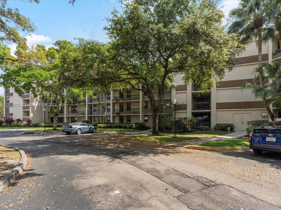 Front view of a multi-story residential building with balconies and surrounding trees.