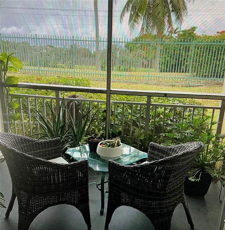 View from a patio with wicker chairs overlooking a fenced area with greenery.