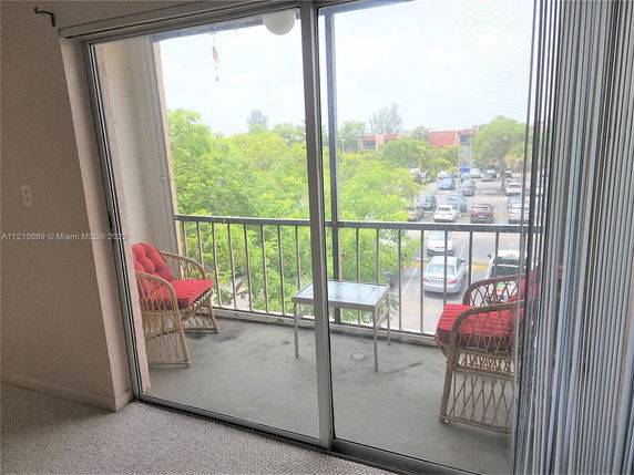 View from a balcony with chairs overlooking a parking area and trees.