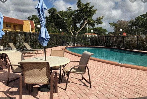 Outdoor swimming pool area with chairs and tables surrounded by a fence.