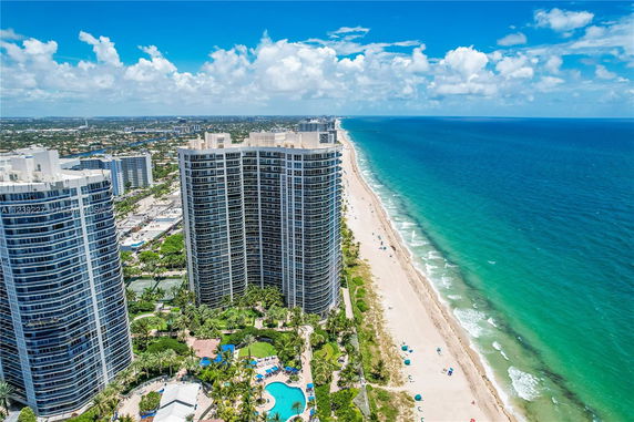 Aerial view of high-rise buildings along a beach shoreline with clear blue waters.