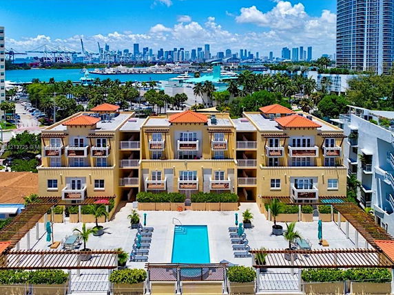 Aerial view of a multi-story residential building with a pool area, located near a waterway and surrounded by other buildings.