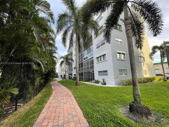 Side view of a multi-story apartment building with a walkway and palm trees.