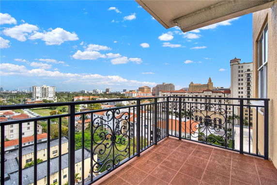 View from a balcony overlooking a cityscape with multiple buildings and a blue sky.