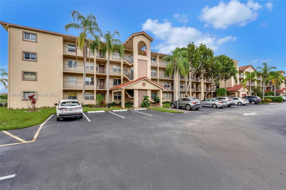 Front view of a multi-story apartment building with balconies and a parking area.