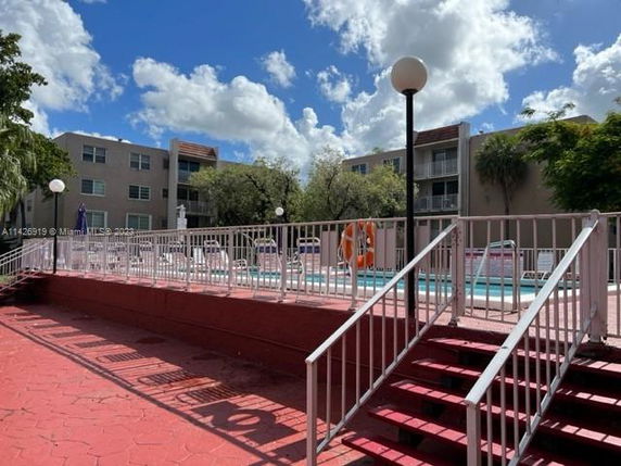 Outdoor swimming pool area with multi-story apartment buildings in the background.