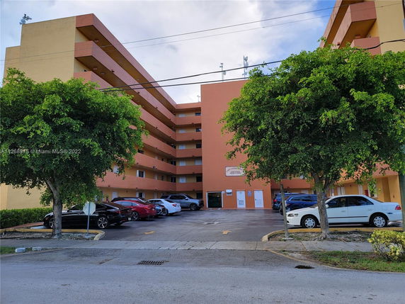 Front view of a multi-story apartment building with parking area in front.