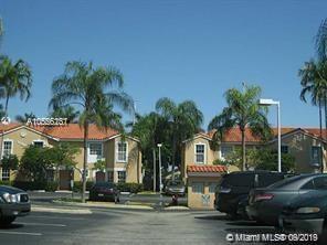 Outdoor view of a parking area with cars in front of a multi-story building with palm trees.