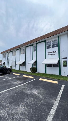 Front view of a two-story building named Cypress Gardens with a sloped roof and parking area.