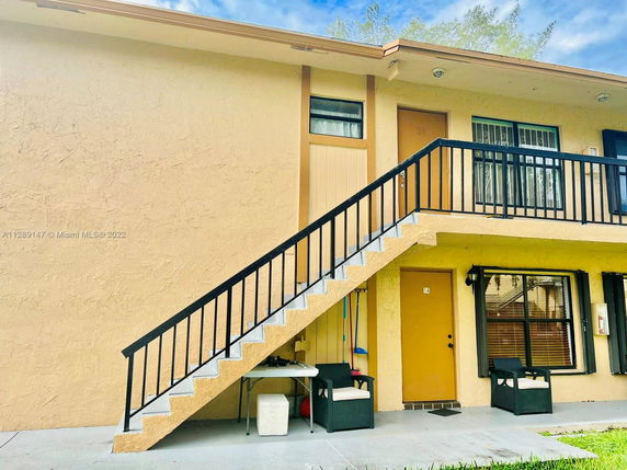 Front view of a two-story building with exterior stairway and seating area.
