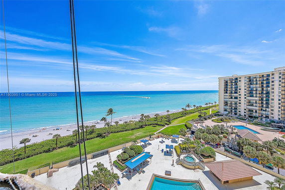 Panoramic view of a coastal area with a sandy beach and ocean, featuring adjacent high-rise buildings and landscaped areas.
