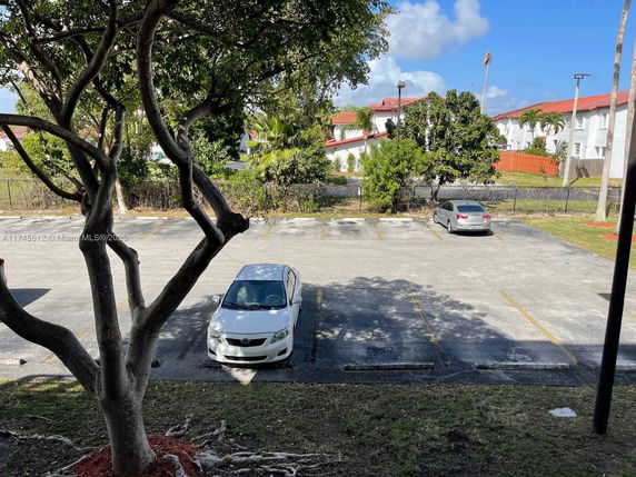 Outdoor parking area with a few cars parked, surrounded by trees and buildings in the background.