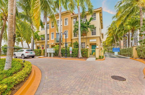 Front view of a three-story residential building with palm trees and a gated entrance.