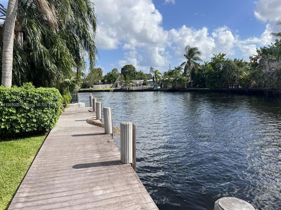 View of a waterfront area with a wooden dock and lush greenery.