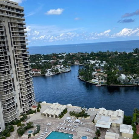 Panoramic view from a high-rise showing a swimming pool, residential areas, and the ocean in the background.