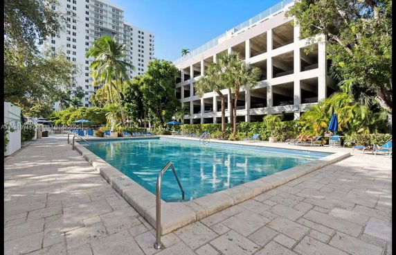 Outdoor swimming pool area with surrounding trees and a building in the background.