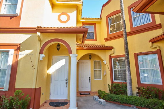 Front view of a two-story building with multiple doorways, arched entryways, and yellow exterior walls.