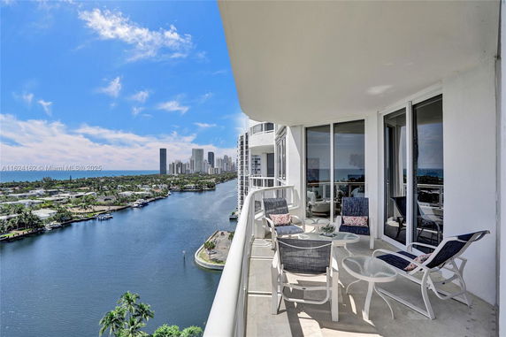 Balcony view showcasing a waterway and city skyline with a seating area.