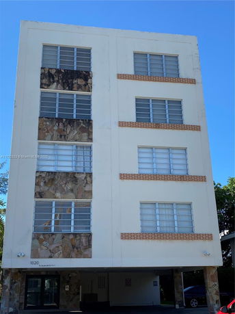 Front view of a four-story residential building with large windows and textured stone accents.