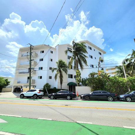 Front view of a multi-story apartment building with balconies and palm trees.