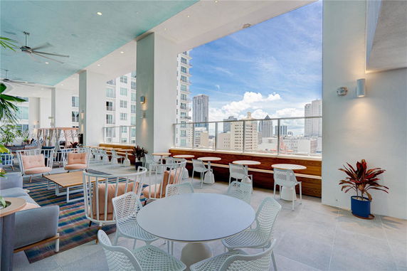 Interior view of a modern club house with seating and tables, overlooking a cityscape.