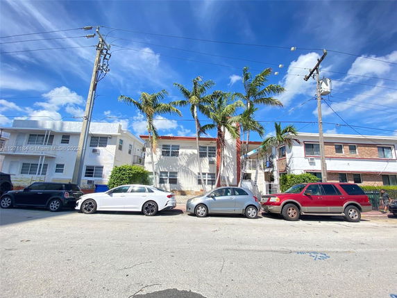 Front view of a two-story residential building with palm trees and parked cars.