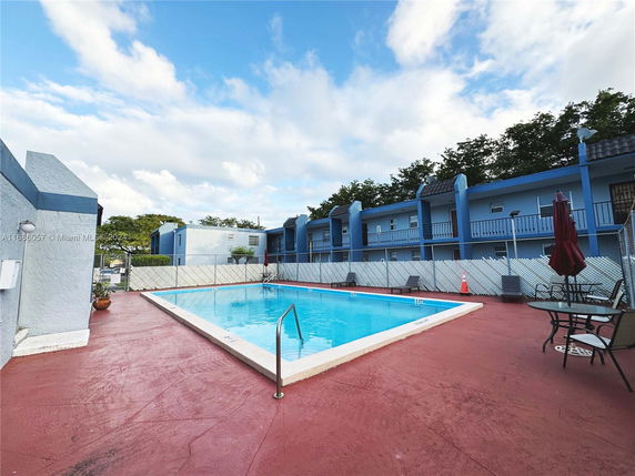 Outdoor swimming pool area with adjacent buildings and lounge chairs.