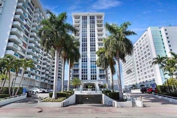 Front view of a high-rise building with palm trees and multiple balconies.