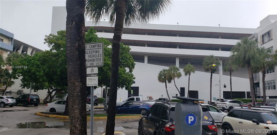 Outdoor parking area with multiple parked cars and a large building in the background.