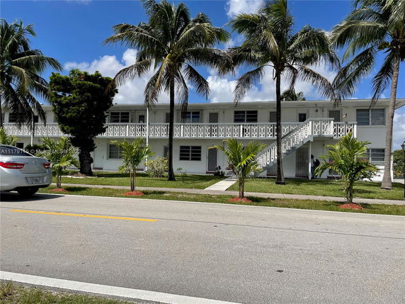 Front view of a two-story building with palm trees and a staircase leading to the upper floor.