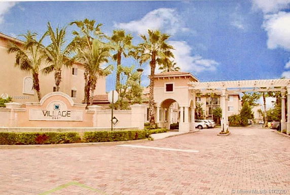 Front view of a residential complex entrance with an archway and palm trees.