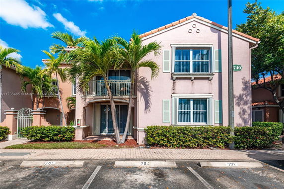 Front view of a two-story house with a balcony and palm trees.