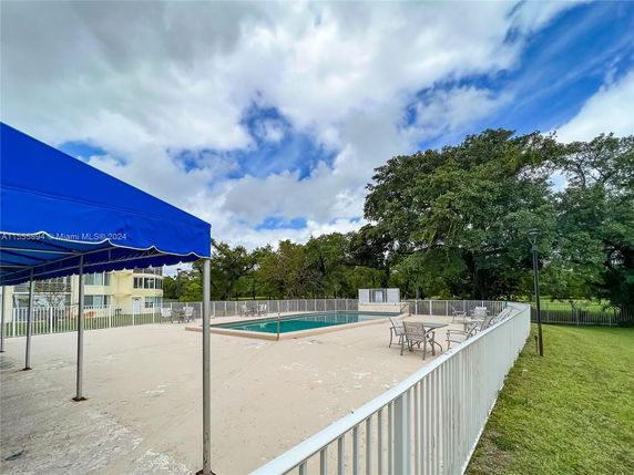 Outdoor swimming pool with a fenced area and nearby seating under a blue canopy.