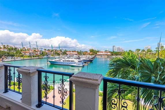 View of a marina with yachts, palm trees, and buildings in the background.