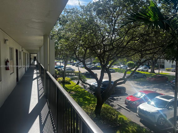 View from a balcony overlooking a parking area with cars and trees.