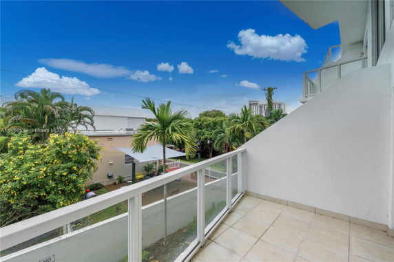Balcony view with railing overlooking palm trees and distant buildings.