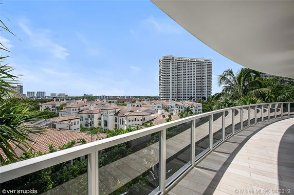 Panoramic view of a cityscape from a curved balcony, featuring a tall building and several residential structures with tiled roofs.