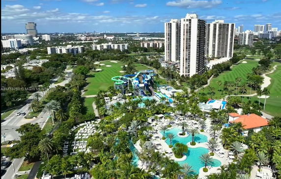 Panoramic view of a cityscape with high-rise buildings, a golf course, and a water park surrounded by lush greenery.