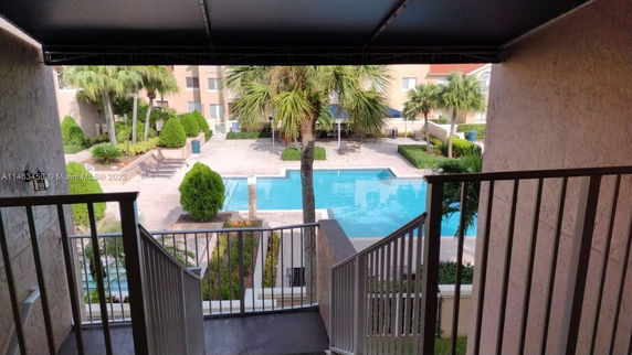View of a swimming pool area with surrounding trees and residential buildings.