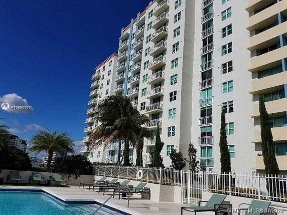 Outdoor swimming pool area in front of a multi-story residential building.