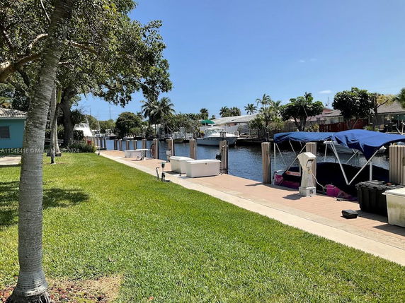 View of a waterfront area with boats docked along a canal and trees on a sunny day.