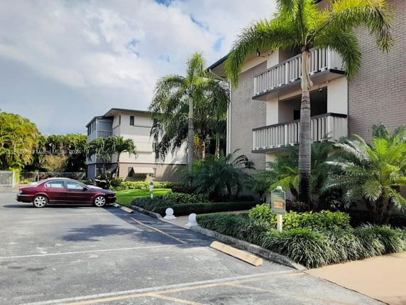 Front view of a multi-story building with balconies and surrounding vegetation.