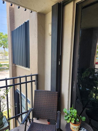 Balcony area with a chair and potted plant, view of nearby buildings and trees.