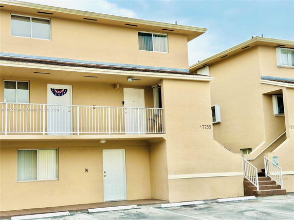 Front view of a two-story apartment building with beige exterior and white railings.