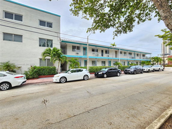 Front view of a two-story building with a row of cars parked in front.