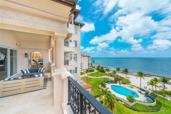 Panoramic view from a balcony overlooking the ocean and landscaped garden with pool.