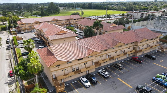 Aerial view of a group of buildings with red-tiled roofs, parking spaces, and surrounding greenery.